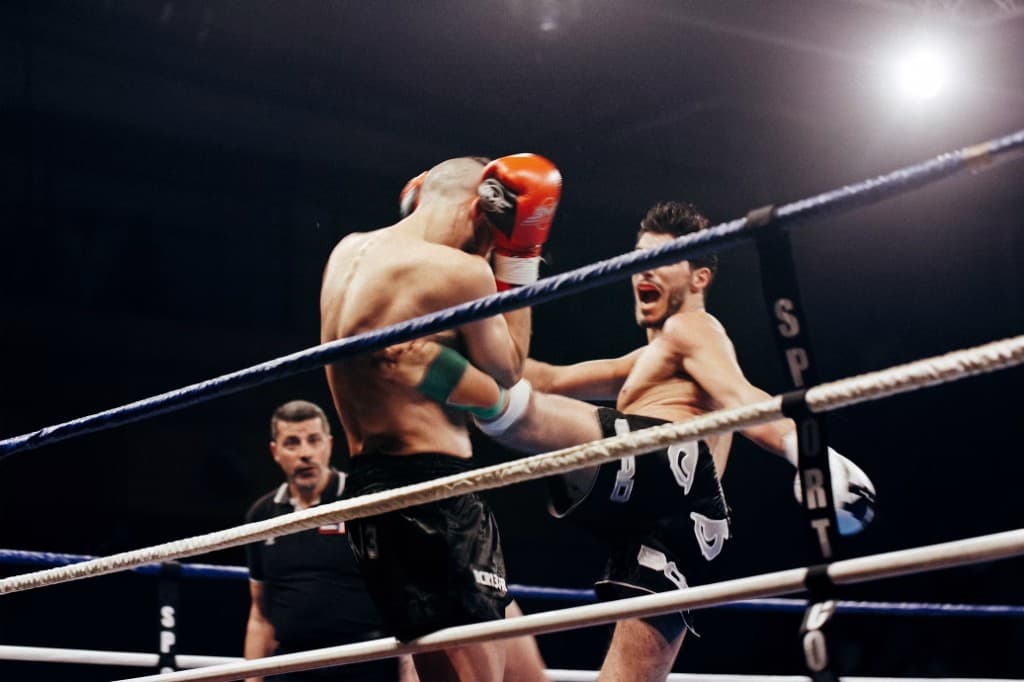 Kickboxer landing a head kick over a high guard, upper body leaning back to stay balanced.